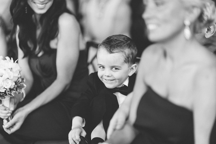 Boy smiles for the camera during a wedding ceremony at Pier 60 & The Lighthouse. Captured by NYC wedding photographer Ben Lau.