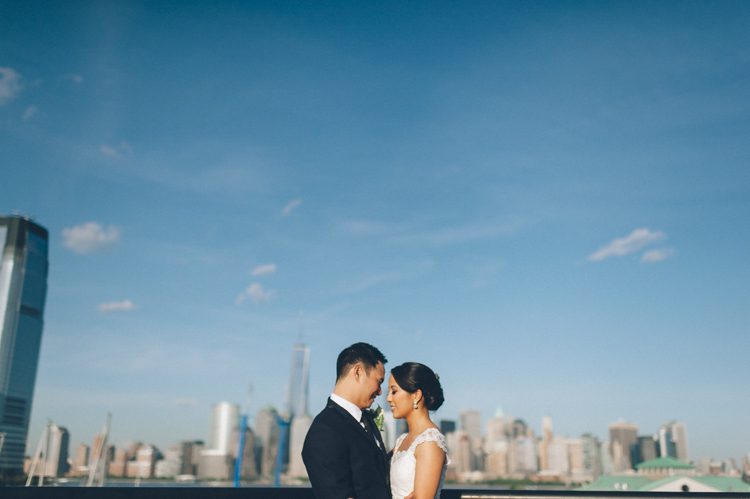 Bride and groom takes a photo with the NYC skyline during their wedding reception at Maritime Parc in Jersey City, NJ. Captured by NYC wedding photographer Ben Lau.