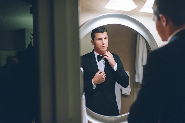 Groom looks at his reflection in the mirror on the morning of his wedding at the Liberty House in Jersey City, NJ. Captured by awesome NJ wedding photographer Ben Lau.