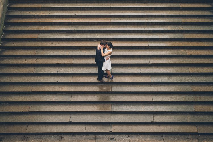 Couple share a kiss on the steps during their engagement session in Central Park. Captured by NYC wedding photographer Ben Lau.