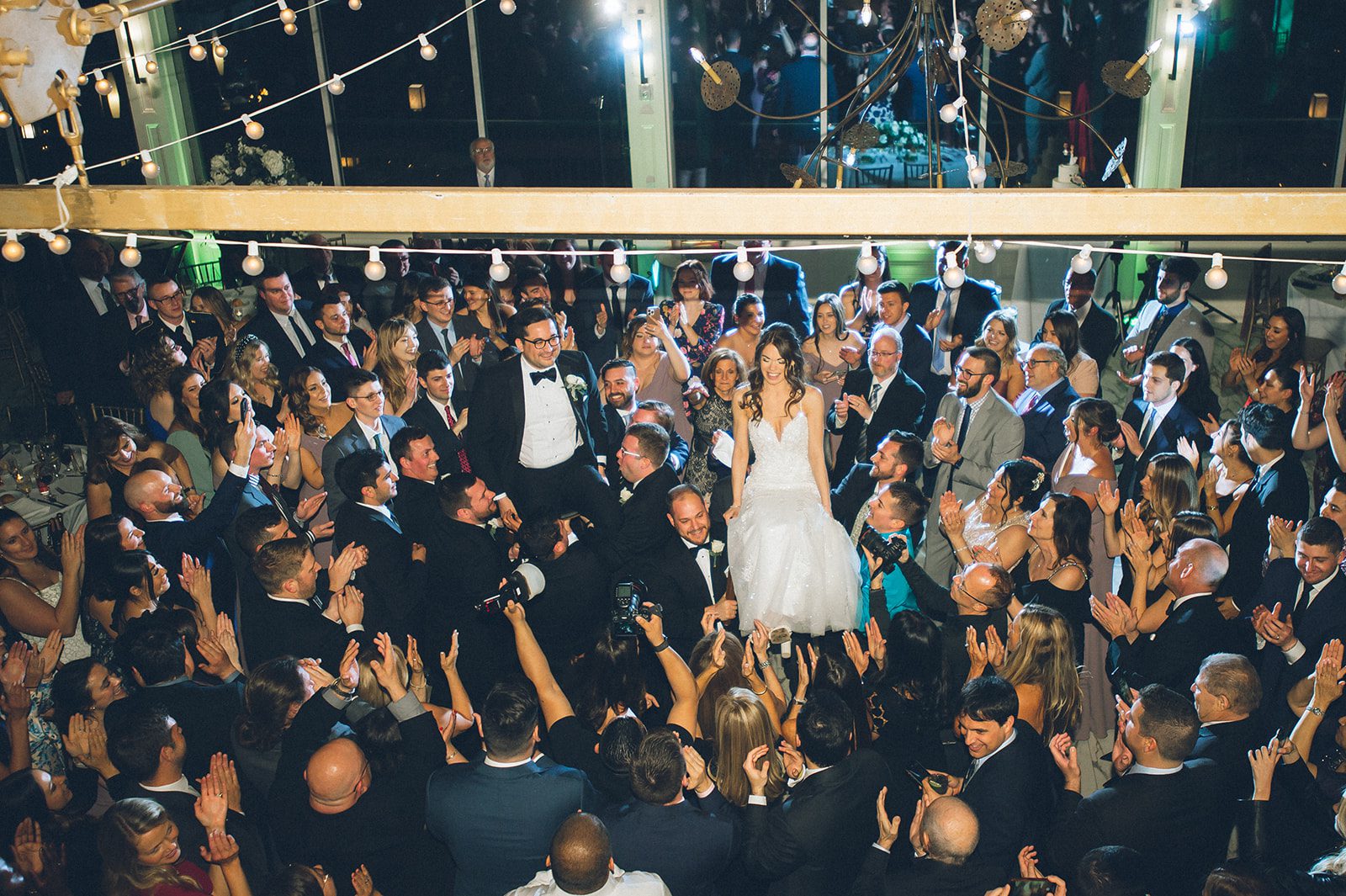 The bride & groom are lifted in the air during a Jewish Horah. This wedding took place at Liberty House, a modern, waterfront wedding venue in Jersey City, which features views of NYC.