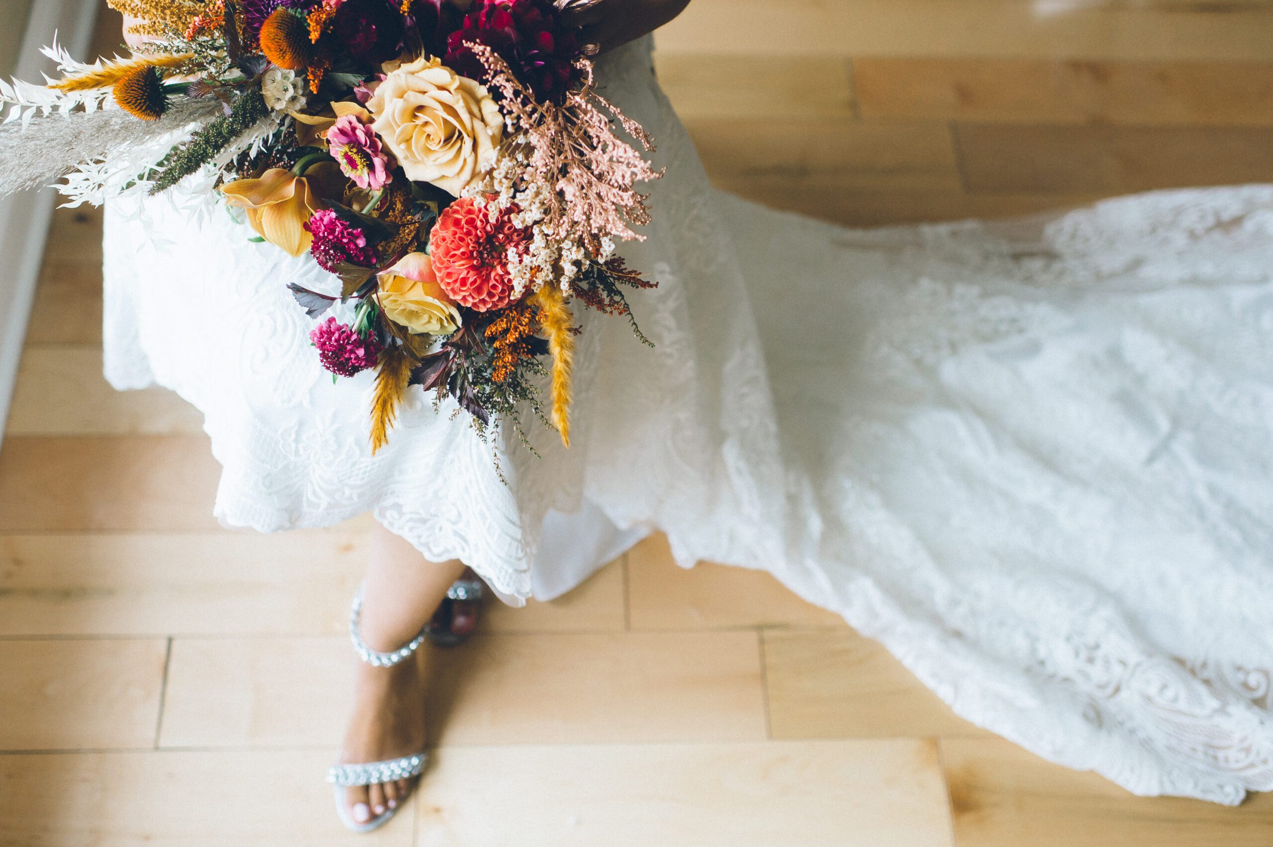 Alliee holding her colorful bouquet beside the lace train of her wedding dress.