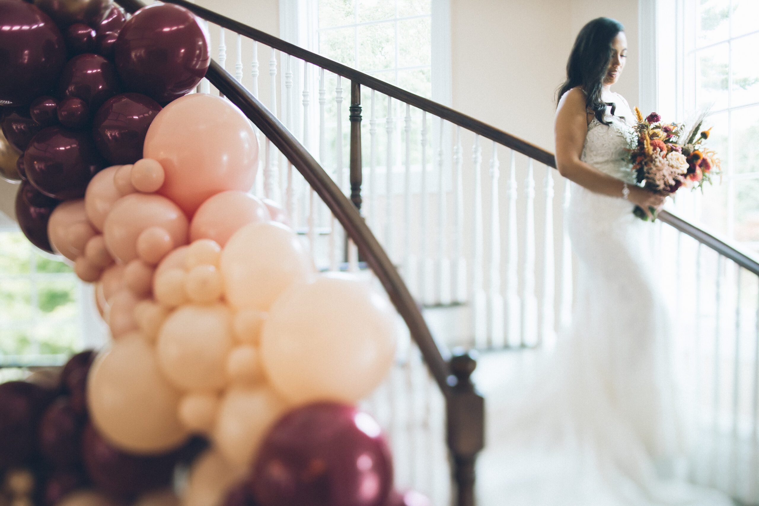 Alliee standing by the staircase with her bouquet and a burgundy balloon installation nearby.
